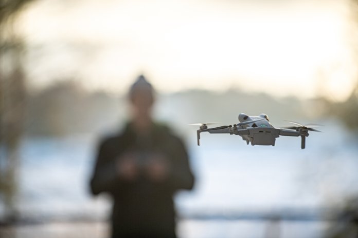 Drone,In,Flight,With,Pilot,In,Background.